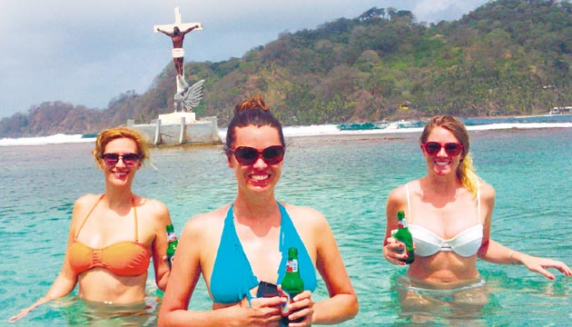 Los visitantes de todas las nacionalidades se bañan en las cristalinas aguas bajo la imagen del Cristo Negro en Isla Grande.