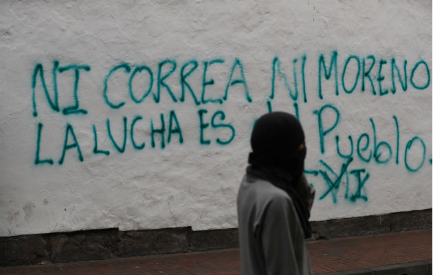 Ecuador decreta el estado de excepción ante protestas por medidas económicas Un encapuchado camina ante una pared con una frase contra el Gobierno. Foto: EFE.