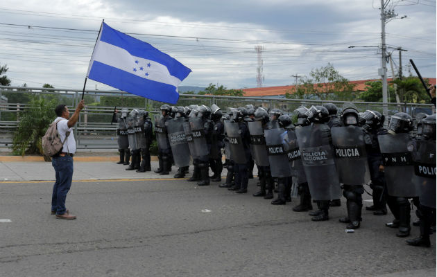 Manifestantes y policías se enfrentan en segundo día de protestas en Honduras Un manifestante ondea una bandera hondureña frente a efectivos de la Policía. EFE.