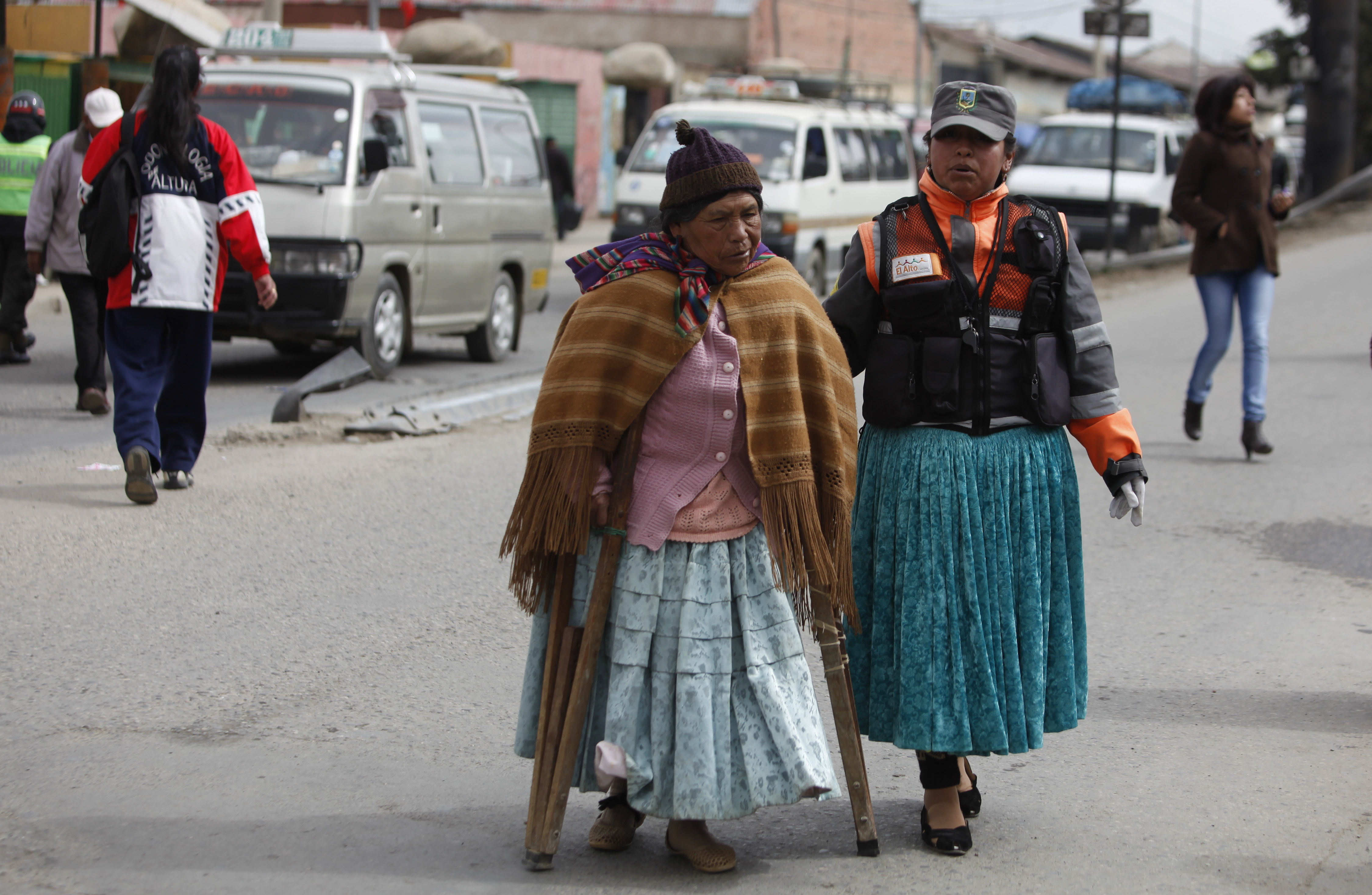 Cholita de tránsito ayuda una a viejita a cruzar la calle. En vez de las gorras normales, usan gorras color ejército, y algunas con chalecos fosforescentes. Foto/AP