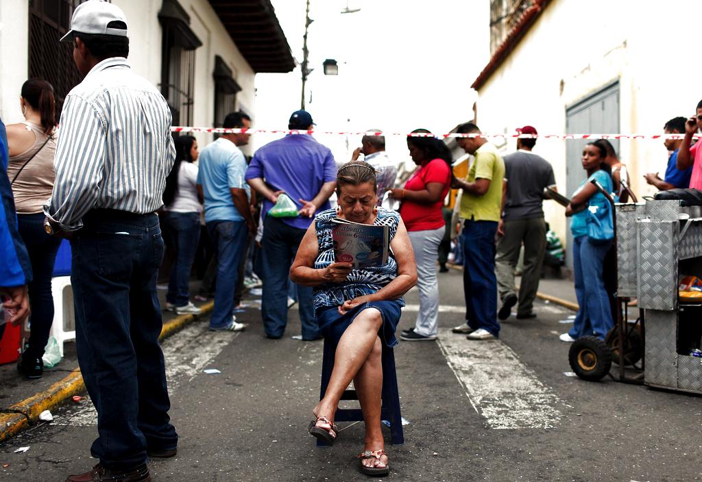Una mujer lee una revista mientras decenas de caraqueños hacen cola. Foto: EFE<br>