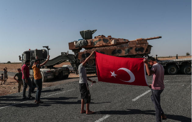 Turquía asegura haber tomado la primera ciudad en la franja kurda de Siria Jóvenes con la bandera turca al paso de blindados militares turcos en el noreste de Siria. Foto: EFE.