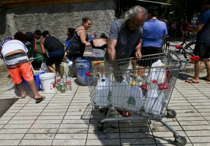 Un grupo de personas consiguen agua del hidrante. FOTO/EFE