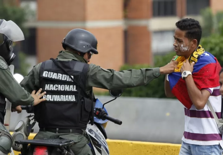 Un policía detiene a un joven. /Foto AP