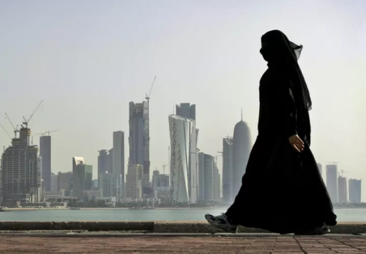 Una mujer camina frente a modernos rascacielos en la ciudad de Doha, en Catar. /Foto AP