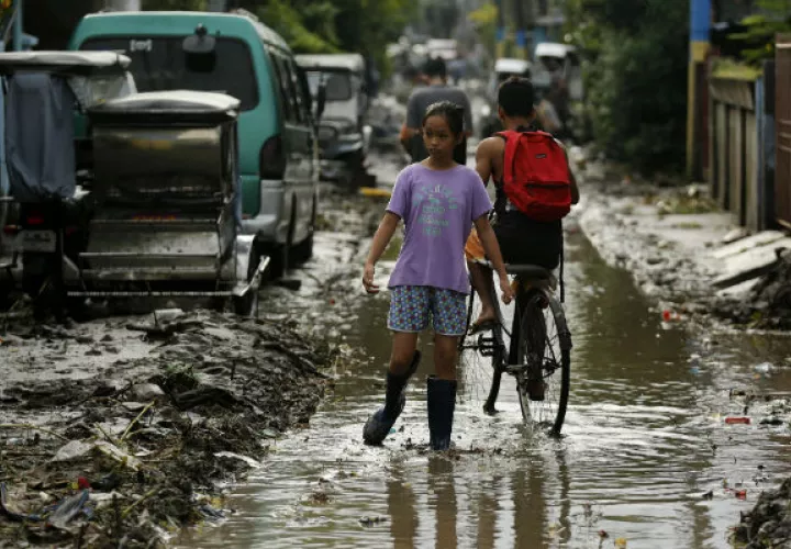 Filipinos transitan por una vía inundada y cubierta de lodo,  debido a las inundaciones. Fotos: EFE 