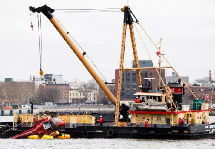 Una grúa saca un helicóptero en el estrecho del East River de Nueva York. EFE