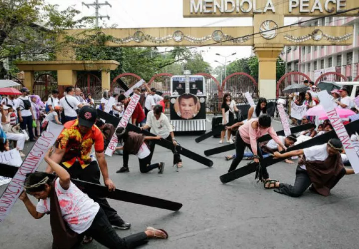 Manifestantes con cruces de madera se arrodillan en el suelo durante una protesta en Manila. Foto: EFE