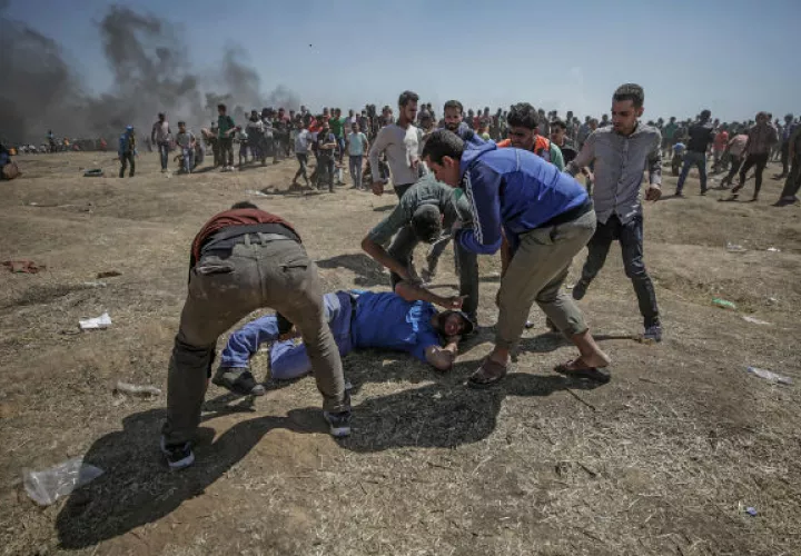 Manifestantes palestinos tratan de ayudar a un herido durante enfrentamientos tras una protesta cerca de la frontera con Israel .FOTO/EFE