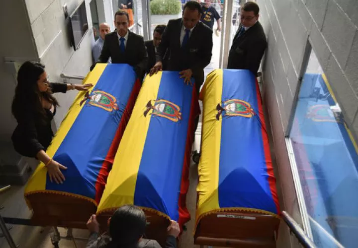 Un grupo de personas coloca banderas de Ecuador sobre los féretros. Foto: EFE