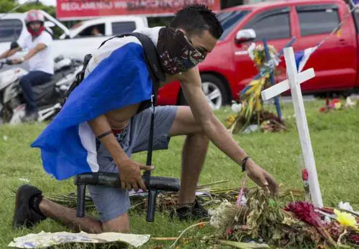 Un joven con una bandera de Nicaragua en la espalda y un lanza morteros en su mano rinde un homenaje en un altar. FOTO/EFE