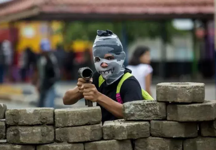 Un joven con la cara tapada y un lanza morteros cuida una barricada en el barrio indígena de Monimbó. EFE