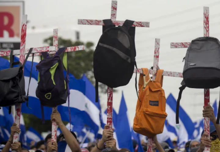 Varios jóvenes con unas cruces con mochilas en honor a los estudiantes que murieron en las pasadas manifestaciones. FOTO/EFE