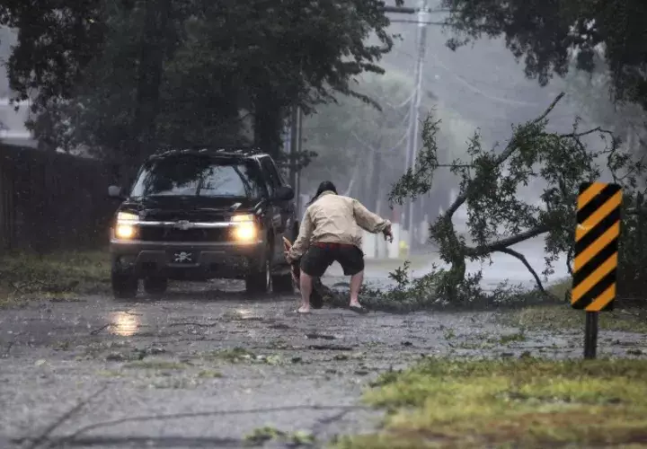 Un hombre mueve un largo árbol que cayó cerca de su auto. AP