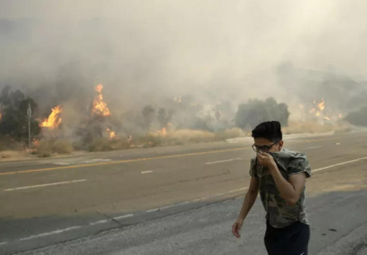 Un joven camina cubriéndose la nariz del humo causado por el fuego en Santa Clarita. Foto: AP.  