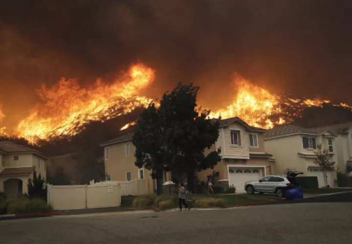 Un joven camina cubriéndose la nariz del humo causado por el fuego en Santa Clarita. Foto: AP.  