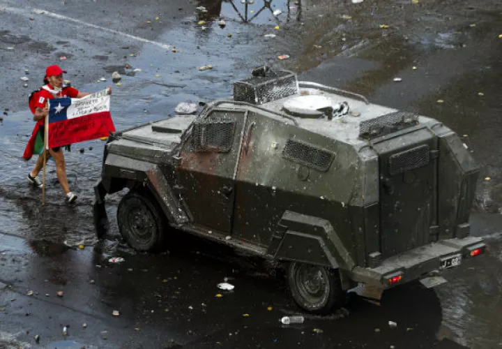 Un manifestante enfrenta con una bandera a un vehículo blindado en Santiago. Foto: AP.