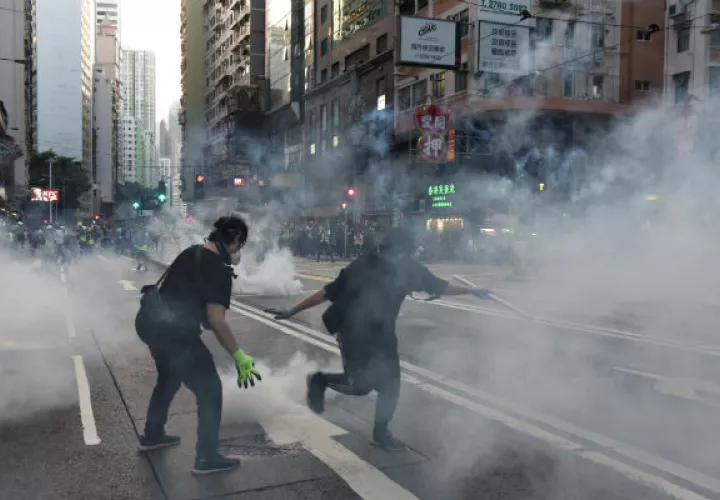 Un hombre afectado por gas pimienta camina ante policías antidisturbios. Foto: EFE.