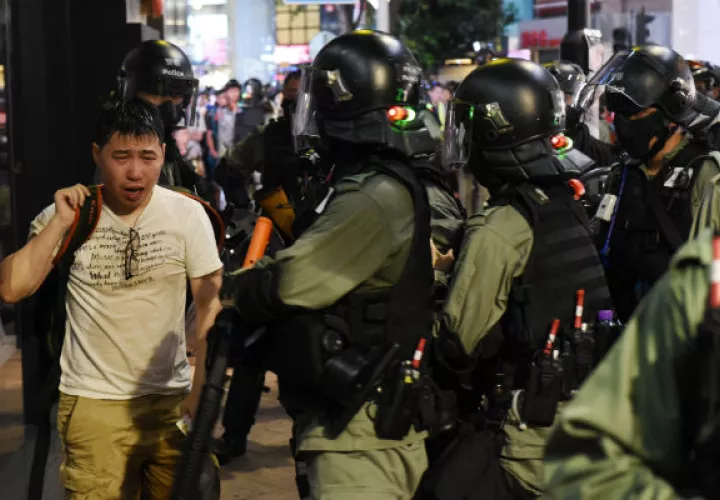 Un hombre afectado por gas pimienta camina ante policías antidisturbios. Foto: EFE.