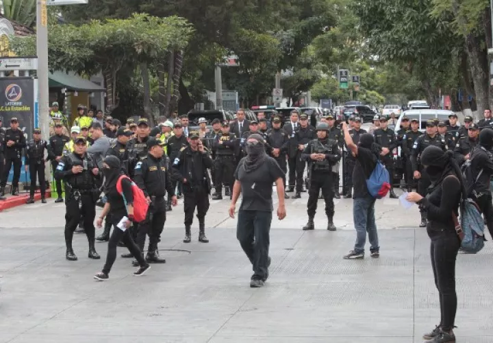 Jóvenes encapuchados son rodeados por miembros de la policía durante una protesta contra la investidura de Alejandro Giammattei FOTO/EFE
