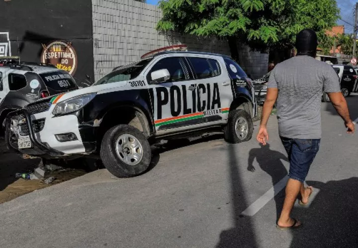 Un hombre encapuchado -supuestamente agente de la policía- camina frente a un vehículo de la institución visiblemente dañado. FOTO/EFE
