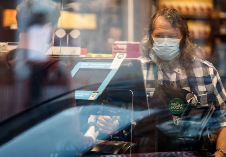 Un empleado de Whole Foods Market con cubrebocas durante la pandemia de coronavirus, frente a una caja registradora, en Washington. (Ting Shen/The New York Times)
