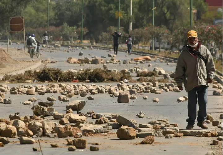 Un hombre cruza un bloqueo de una carretera durante las protestas en Cochabamba. Fotos: EFE.