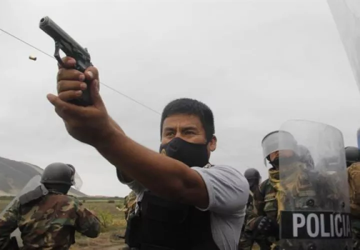 Un miembro de la Policía mientras apunta su arma a manifestantes durante una protesta de trabajadores agroindustriales 