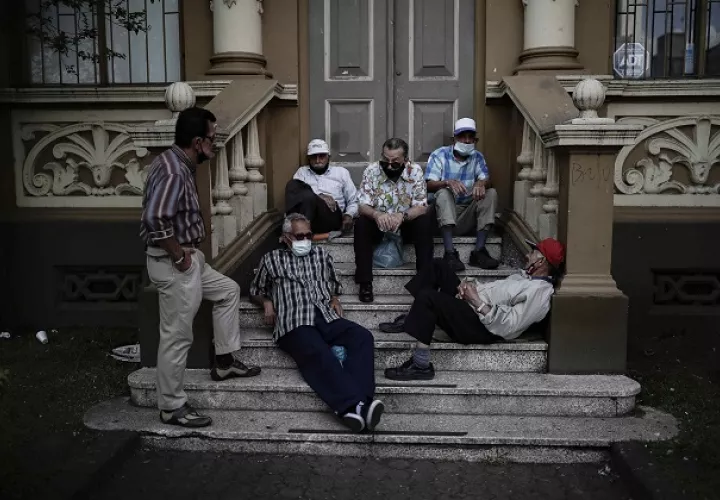  Varios hombres, algunos sin el uso correcto del tapabocas, conversan en las escalinatas de un edificio en una calle de San José, Costa Rica. Foto: EFE
