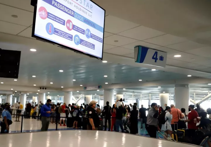 Pasajeros aguardan en cola para pasar las medidas de seguridad del covid-19 en el Aeropuerto Luis Muñoz Marín en San Juan.
