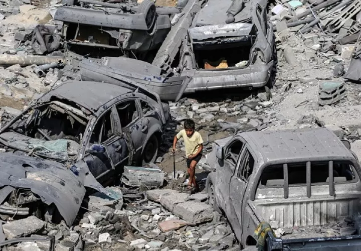 Un niño palestino pasa junto a coches dañados en los ataques aéreos israelíes en la ciudad de Gaza. Foto: EFE/Mohammed Saber