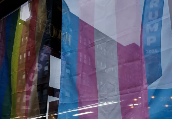 Fotografía de archivo de banderas alusivas a Donald Trump que se reflejan en una ventana que muestra banderas del Orgullo LGBTQ. Foto: EFE