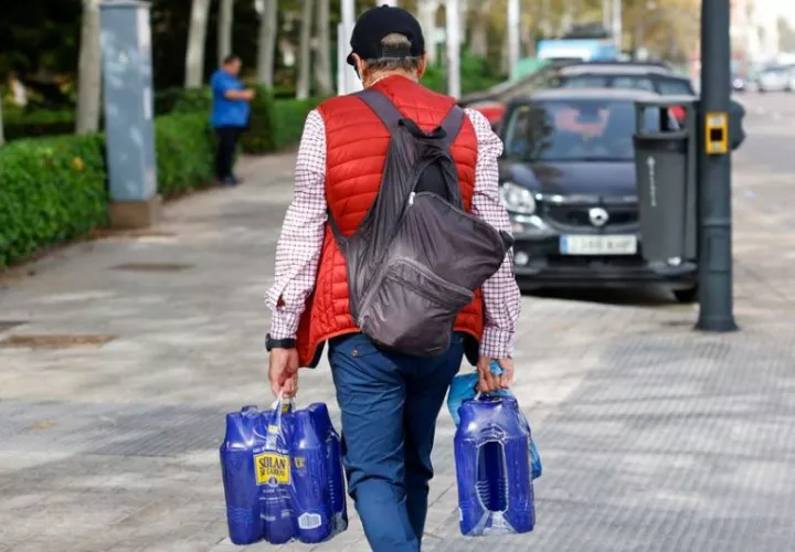 Un hombre carga con varias botellas de agua en Valencia. Foto: EFE