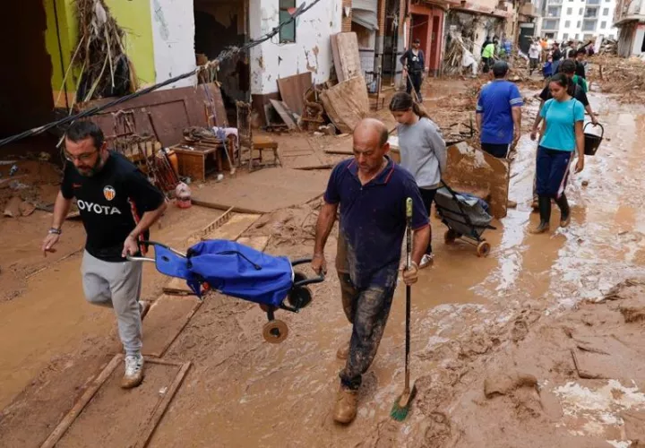 Vecinos cruzan una calle llena de fango y escombros en la localidad de Paiporta este sábado tras el paso de la DANA. Foto: EFE