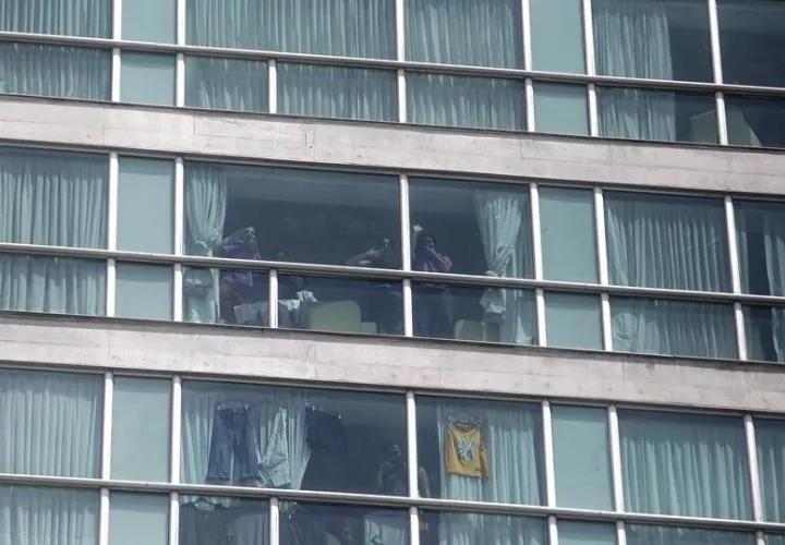 Migrantes hacen señas desde una ventana del hotel Decápolis este martes en Ciudad de Panamá, donde se mantienen tras ser deportados de EE.UU. Foto: EFE