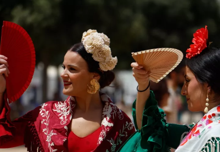 Varias mujeres vestidas de flamenca se cubren los ojos con abanico. Foto: EFE / Salas