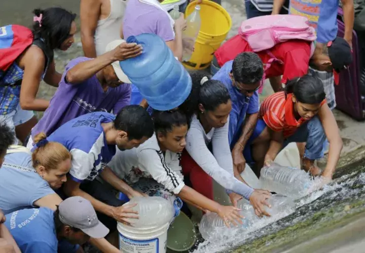 Venezolanos recogen agua de una tubería rota cerca al río Guaire, en Caracas. AP