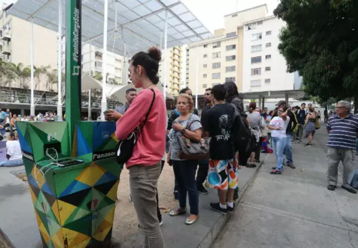 Personas hacen fila para recargar la batería de sus teléfonos móviles en un punto público durante el apagón eléctrico en Caracas. Foto: EFE.