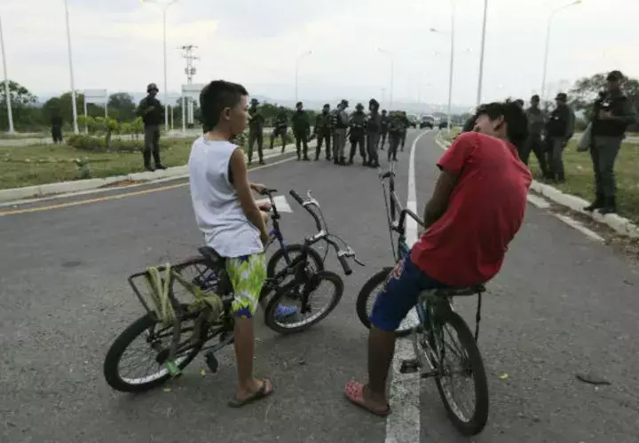 Dos niños en bicicleta frente a soldados venezolanos que bloquean el paso por el puente internacional de Tienditas. Foto: AP