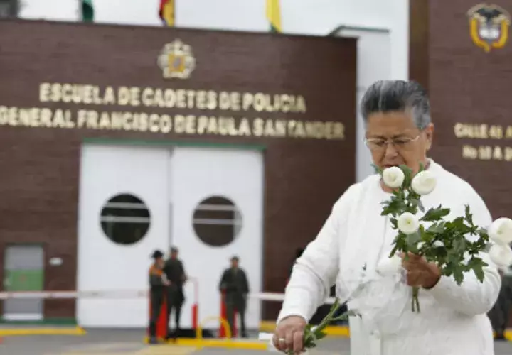 Una mujer porta flores ante la academia atacada con explosivos. Foto: EFE.