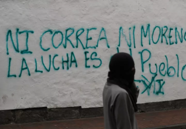 Un encapuchado camina ante una pared con una frase contra el Gobierno. Foto: EFE.