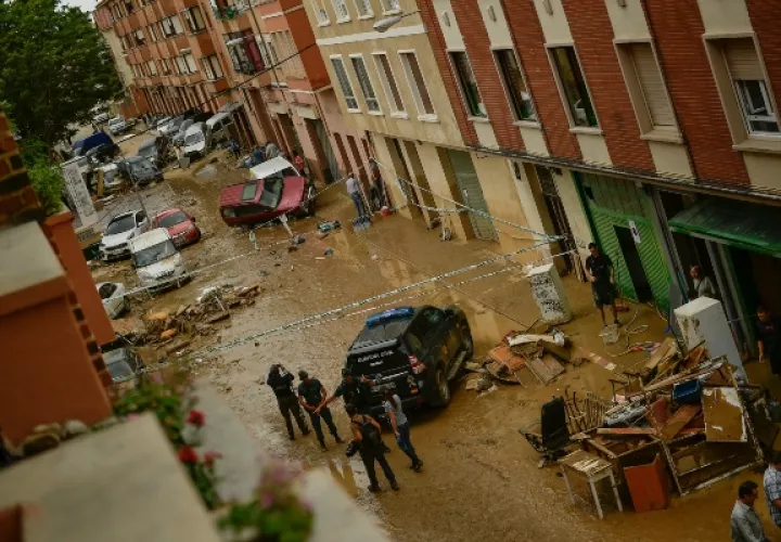 Los residentes caminan en la calle junto a los autos dañados después de las fuertes lluvias en Tafalla, en el norte de España. FOTO/AP