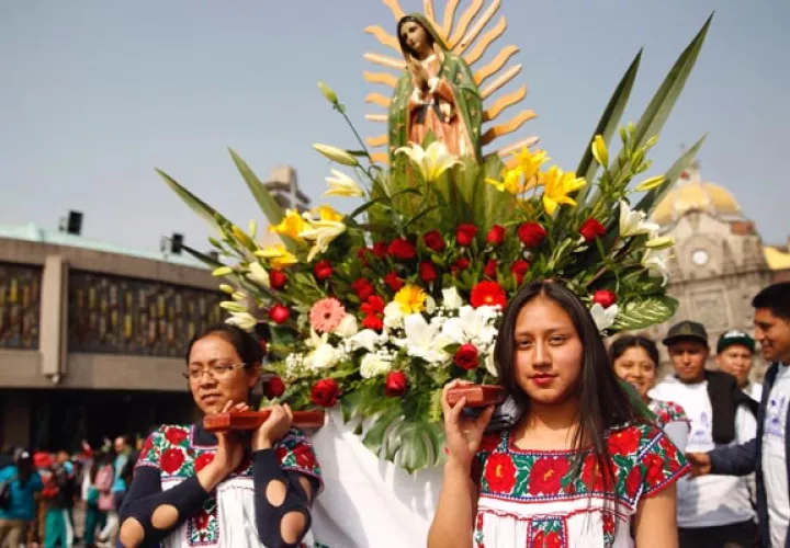Dos jóvenes cargan una corona de flores con la imagen de la virgen de Guadalupe. FOTO/EFE