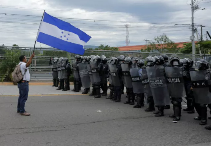 Un manifestante  ondea una bandera hondureña frente a efectivos de la Policía. EFE.