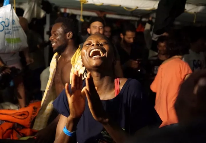 Varios migrantes esperan en el barco de la ONG española Open Arms, que sigue bloqueado desde hace 19 días frente a la isla italiana de Lampedusa. El buque militar español Audaz zarpó esta desde la base de Rota hacia Lampedusa para recoger y acompañar a España a los inmigrantes del Open Arms, casi de manera simultánea a que un fiscal italiano decretara su desembarco inmediato en la isla italiana y la incautación de la nave humanitaria. FOTO/EFE