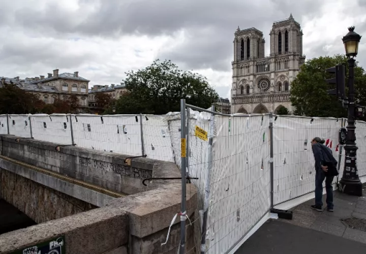 Los turistas miran a través de paneles de protección que aseguran un perímetro alrededor de la Catedral de Notre Dame antes del inicio de un tratamiento masivo de descontaminación de plomo alrededor del monumento, en París.FOTO/AP