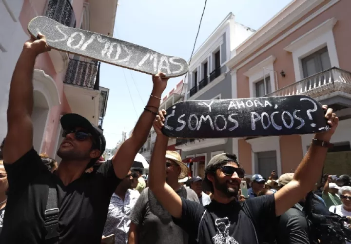  Manifestantes que esperan la renuncia del gobernador de Puerto Rico sostienen pancartas que dicen "Y ahora, ¿somos pocos?" y "Somos más" este miércoles durante el decimotercer día de protesta frente a La Fortaleza, sede del Ejecutivo, en el Viejo San Juan, Puerto Rico. FOTO/EFE