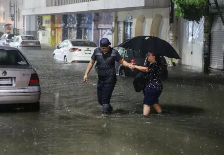  Dos personas cruzan una calle inundada en el puerto de Acapulco por el huracán Rosa. 