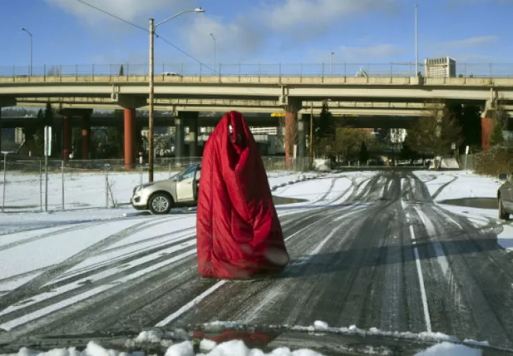 Un hombre camina por la calle cubierto con una bolsa de dormir ante el intenso frío en Portland, Oregon.  Foto: AP.